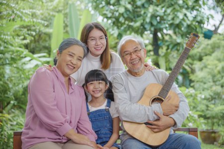 Téléchargez les photos : Famille heureuse Asiatique senior homme ou grand-père jouer de la guitare tandis que sa grand-mère et sa petite-fille chantent ensemble à l'extérieur à la maison, Activité famille, Profiter de style de vie senior plus âgé - en image libre de droit