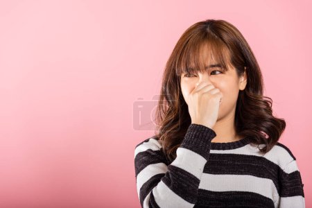 Téléchargez les photos : Une femme asiatique malheureuse se serre le nez avec dégoût à cause d'une odeur nauséabonde. Studio tourné isolé sur fond rose, reflétant le concept de santé. - en image libre de droit