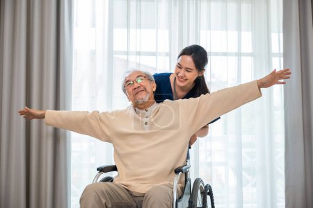 Téléchargez les photos : Heureux curateur personne médecin poussant et marcher la liberté des patients âgés levant le bras à l'hôpital, asiatique retraité vieil homme assis sur fauteuil roulant s'amuser avec une jeune infirmière, sanatorium handicapé - en image libre de droit