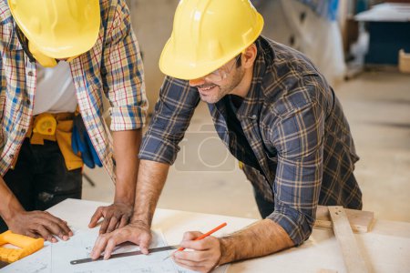 Photo for Craftsmen sketch of future project on blueprint paper in woodshop, Carpenter man wear helmet meeting planning a job together at carpentry workshop, team discuss, National Carpenters Day - Royalty Free Image