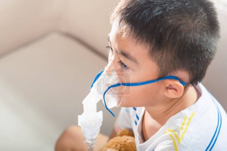 Téléchargez les photos : Asian Child using nebulizer mask equipment alone have smoke, Kid boy making makes inhalation nebulizer steam sick cough at home, oxygen spray inhaler therapy, stuffy nose and runny, Health medical - en image libre de droit