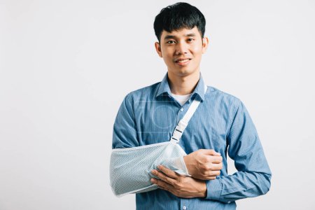 Photo for Injured businessman remains confident while dealing with broken arm, utilizing splint for treatment. happy Asian man in sling for support, on white background, signifying path to recovery. Copy space - Royalty Free Image