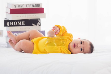 Photo for Asian cute baby little girl toddler looking at a stack of books on bedroom white bed, First baby library concept - Royalty Free Image