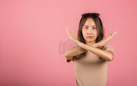 Téléchargez les photos : Portrait Asian beautiful young woman unhappy or confident standing holding two cross arms say no X stop sign, studio shot isolated pink background, Thai female pose reject gesture with copy space - en image libre de droit