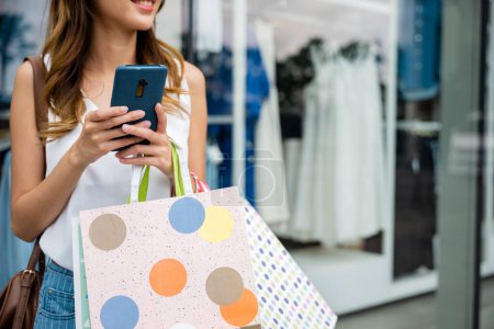 Photo for A fashionable woman multitasking with shopping bags and a cellphone enjoys the convenience of online shopping. Shes browsing the latest fashion and accessories while on the go. - Royalty Free Image