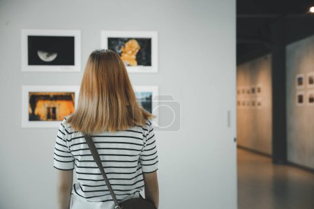 Foto de Asian young woman standing she looking art gallery in front of colorful framed paintings pictures on white wall, female watch at photo frame to leaning against at exhibit museum, Back view - Imagen libre de derechos