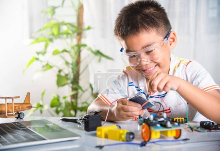 Téléchargez les photos : Enfant asiatique garçon branchant l'énergie et le câble de signal à la puce de capteur avec la voiture robot Arduino, Petit enfant apprendre à distance en ligne avec jouet de voiture, cours de technologie d'IA d'éducation STEAM leçon d'apprentissage scolaire - en image libre de droit