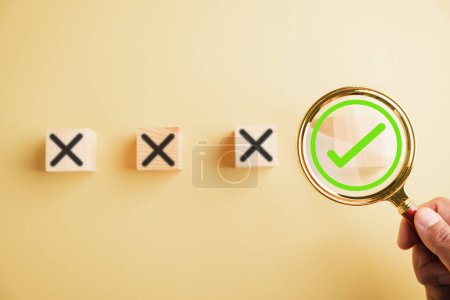 Photo for Hand holding a magnifying glass focuses on the right choice concept, with a checkmark or tick symbol next to wrong cross icons. Emphasizing the importance of making the correct decision. - Royalty Free Image