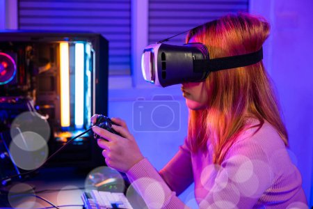 Photo for Gamer in VR headset glasses exploring metaverse play video game online with joystick on computer neon lights, Excited woman virtual playing gamepad controller she celebrating victory at home - Royalty Free Image