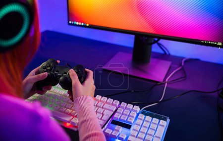 Photo for Woman wear gaming headphones playing live stream esports games console at home, Gamer using joystick controller for virtual tournament plays online video game with computer neon lights - Royalty Free Image