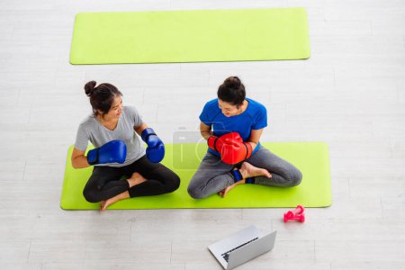 Téléchargez les photos : Overhead style de vie asiatique adulte et jeune femme sport fitness boxer portant des gants sur la boxe dans les vêtements de sport regarder ordinateur portable pour l'entraînement studio de yoga en ligne, sport sain concept d'entraînement - en image libre de droit