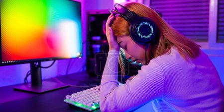Foto de Game over you lose. Angry Asian gamer wearing gaming headphones playing joystick console video game on computer PC neon light at home feeling sad disappointed about game losing, player unhappy E-Sport - Imagen libre de derechos