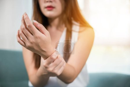 Photo for Closeup hand. Asian woman hand problem injury feeling joint pain, young female sitting on sofa holds suffering her wrist at home, performing self-massage, Health care and medical concept - Royalty Free Image