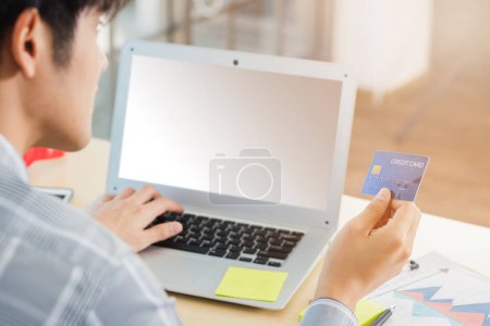 Téléchargez les photos : Asiatique homme d'affaires main tenant carte de crédit et dactylographier entrer le code de sécurité sur un ordinateur portable pour le processus de paiement en ligne achats sur Internet au bureau à domicile - en image libre de droit