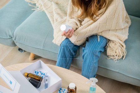 Photo for Asian young woman reading ingredient and hold bottle of drug on sofa at home, sick people reading information medicine label pills, female with flu virus, Health care and medicine concept - Royalty Free Image