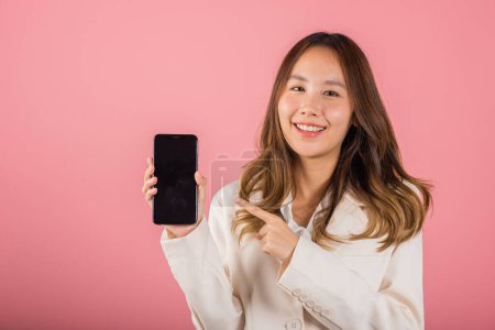 Photo for Portrait Asian happy beautiful young woman smile making finger pointing on screen smartphone in hand shopping online application looking to camera, studio shot isolated pink background with copy space - Royalty Free Image