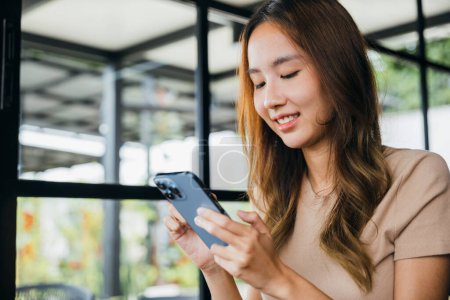 Foto de Mujer joven asiática que utiliza el teléfono inteligente para ir de compras en línea en la cafetería de la cafetería por la mañana, la mujer tiene transferencia de dinero banca financiera por Internet en el teléfono móvil - Imagen libre de derechos