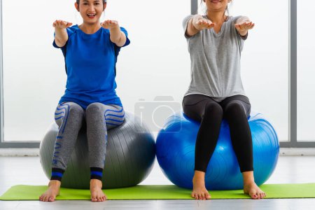 Téléchargez les photos : Two Asian adult and young woman in sportswear doing aerobics yoga exercise with sitting on fitness ball indoor yoga studio, fit sport healthy workout lifestyle exercise - en image libre de droit