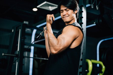 Téléchargez les photos : Un jeune Asiatique fait un câble triceps tirer vers le haut avec un poids lourd lors d'un entraînement de musculation dans la salle de gym. style de vie et concept de personnes - en image libre de droit