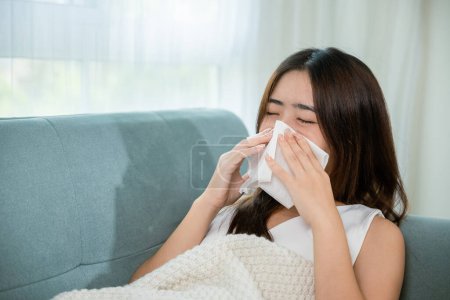 Photo for People sick. Ill Asian young woman cold covered with blanket lying on sofa and sneeze with tissue paper at home, Female sick allergic blowing nose sneezing in tissue at home, Flu health care - Royalty Free Image