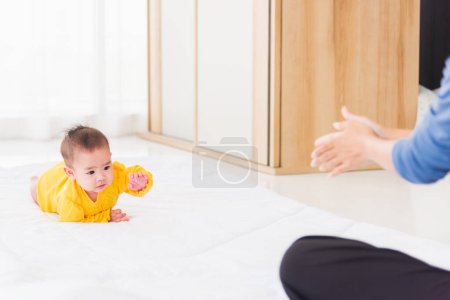 Photo for Asian happy young mother have fun learn walking crawling his daughter baby indoors bedroom at home. The mom playing with her little baby to crawl, two family - Royalty Free Image