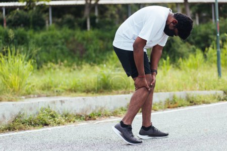 Téléchargez les photos : Asiatique jeune athlète sportif coureur noir homme stand porter pieds chaussures entraînement de course active à l'extérieur, il utilise les mains tenir sur sa douleur au genou lors de la course, sain exercice blessure arthrose de l'entraînement - en image libre de droit