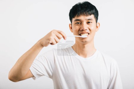 Téléchargez les photos : Un jeune homme asiatique souriant fait preuve d'une brosse à dents appropriée pour la santé dentaire. Studio tourné isolé sur fond blanc, favorisant les soins buccodentaires et la dentisterie. - en image libre de droit