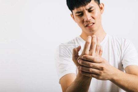 Photo for An Asian man, in pain, massages his painful hands and palms. Portrait in a studio shot isolated on white background, highlighting health care and the concept of arthritis. - Royalty Free Image