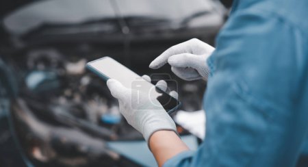 Photo for Skilled repairman using smartphone to diagnose car issues at garage. Close up of mechanics hand holding wrench while examining engine. Horizontal photography with workshop background. - Royalty Free Image