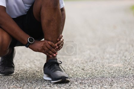 Téléchargez les photos : Gros plan Asiatique jeune coureur de sport noir homme porter montre mains articulaires tenir jambe douleur en raison de la cheville tordue cassé lors de la course au parc de santé de la rue en plein air, exercice sain Blessure de l'entraînement - en image libre de droit