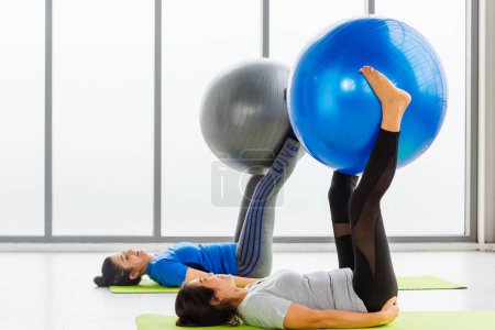 Foto de Two Asian adult and young woman in sportswear doing aerobics yoga exercise abdominal with fitness ball indoor yoga studio, fit sport healthy workout lifestyle exercise - Imagen libre de derechos