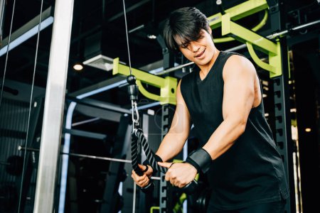 Téléchargez les photos : Bodybuilder qui tire des câbles pour travailler sur ses triceps et construire un haut du corps musclé et puissant, à l'aide d'une machine à câble au centre de remise en forme. Exercice de force du haut du corps - en image libre de droit