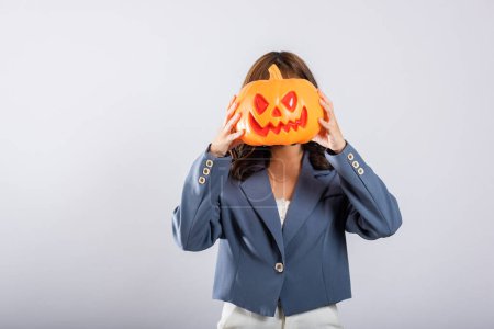 Téléchargez les photos : Femme asiatique met en valeur son esprit Halloween en ornant sa tête d'une citrouille orange tout en embrassant la présence ludique de citrouilles fantômes, évoquant joie et excitation. Concept Halloween Day - en image libre de droit