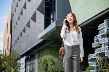 Téléchargez les photos : Jeune avocate femme d'affaires marche rue appel extérieur et parler sur téléphone mobile avec le client, heureux gens sourire parler sur smartphone, communication de téléphone portable - en image libre de droit