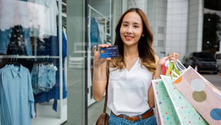 Foto de Una joven sonríe con bolsas de la compra y una tarjeta de crédito en la mano. Ella es una comprador inteligente que sabe cómo encontrar las mejores ofertas y recompensas en el centro comercial. - Imagen libre de derechos