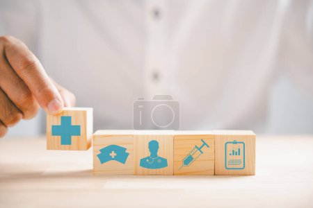 Photo for Symbolic image, Hand grips wooden block displaying healthcare and medical icons. Signifying safety, health, and family well-being, and symbolizing pharmacy, heart care, and happiness. - Royalty Free Image