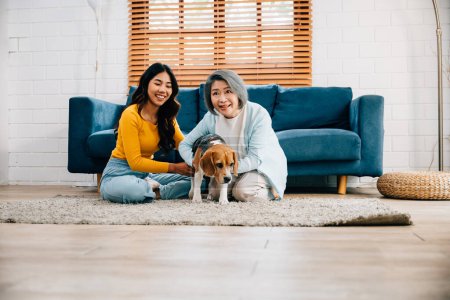 Foto de Activa y saludable, Una mujer y su madre se divierten con su perro Beagle, corriendo cerca del sofá en su cómoda sala de estar. Es una actividad de ocio de fin de semana llena de felicidad. amor mascota - Imagen libre de derechos