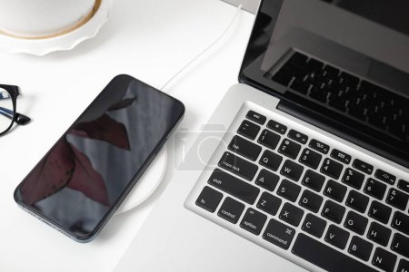 Photo for Charging smartphone battery with wireless charger device near laptop computer, Modern technology transfer energy mobile phone on workspace desktop at home office - Royalty Free Image