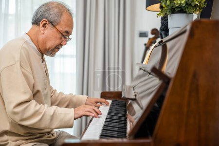 Téléchargez les photos : Homme retraité asiatique apprenant à jouer du piano à la maison, Vieil homme jouant de la musique au piano dans le salon à la maison, mode de vie après la retraite, doigts touchant au clavier - en image libre de droit