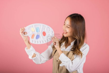 Photo for Asian beautiful young woman artist holding brush and paint palette, Happy female painting using paintbrush and palette with colors, studio shot isolated on pink background, Paintings and art equipment - Royalty Free Image