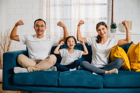 Photo for In their cozy living room a family day concept unfolds as young parents their child and daughter highlight their biceps muscles showcasing strength and togetherness with smiles and joy. - Royalty Free Image
