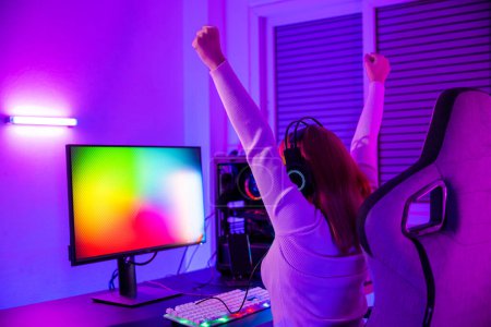 Photo for Winning Victory. Asian gamer playing online video game excited on desktop computer PC colorful neon LED lights, woman in gaming headphones use computer she happy successful, E-Sport concept, back view - Royalty Free Image