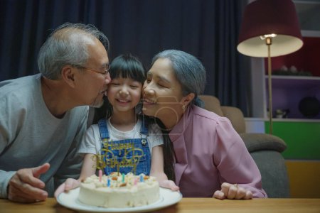Photo for Happy Birthday. Asian family grandfather and grandmother kissed granddaughter feeling thankful while celebrating his birthday after giving wonderful cake, senior family party with child at home - Royalty Free Image