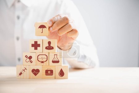 Photo for Hand grips wooden block adorned with healthcare and medical icons, symbolizing safety, health, and family well-being. Reflecting pharmacy, heart care, and happiness. health care concept - Royalty Free Image