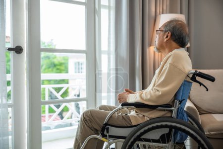 Photo for Asian senior man disabled sitting alone in wheelchair looking through window at hospital, lonely elder thoughtful sad old man look outside windows in bedroom at retirement home, feel depressed lonely - Royalty Free Image