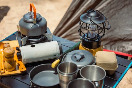Photo for Camping essentials neatly arranged at a beachfront tent, kettle, pot, pan, gas stove, flashlight, and camera. Perfect setup for a relaxing outdoor journey in nature. - Royalty Free Image