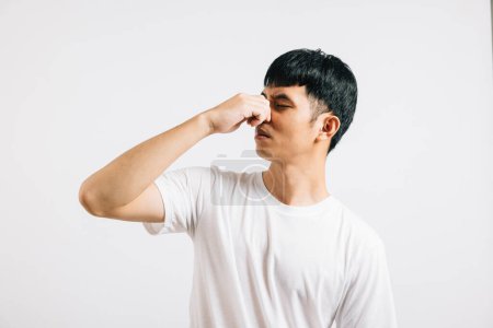 Photo for Portrait of a displeased young man squeezing his nose with fingers, reacting to a gross and smelly odor. Studio shot isolated on white, capturing his strong reaction to the smell. - Royalty Free Image