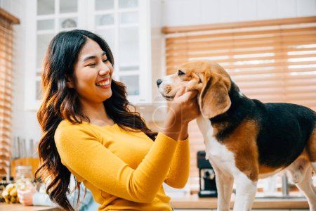 Photo for A playful scene unfolds in the kitchen, where a young Asian woman and her Beagle dog share moments of joy. Their smiles reflect the enjoyment, togetherness, and fun of their friendship. Pet love - Royalty Free Image
