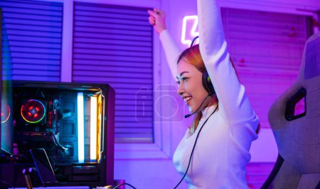 Téléchargez les photos : Victoire victorieuse. Joueur asiatique jouant jeu vidéo en ligne excité sur ordinateur de bureau PC coloré néon LED lumières, jeune femme dans les écouteurs de jeu en utilisant l'ordinateur elle heureux succès, concept E-Sport - en image libre de droit