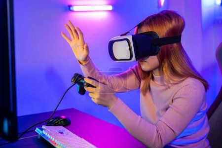 Téléchargez les photos : Gamer en VR lunettes casque explorer métaverse joue jeu vidéo en ligne toucher quelque chose sur l'air et tenir joystick, Femme excitée jouer à regarder la simulation de la vie vidéo à la maison - en image libre de droit